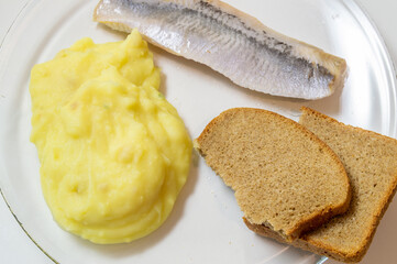mashed potatoes with salted herring and bread on a glass plate