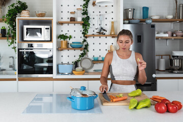 Smiling young sporty woman cooking salad, cutting fresh vegetables in modern kitchen, happy satisfied female preparing vegetarian snacks, food for dinner or party, enjoying leisure time, hobby