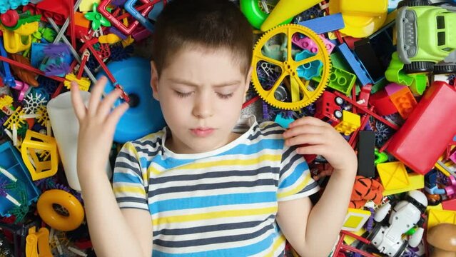 Sad offended little boy throws away a toy lying down among a variety of toys view from above
