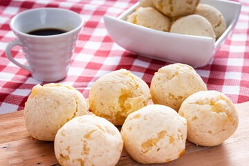 Delicious cheese bread, a typical Brazilian dish, on a wooden board and a checkered tablecloth. Next to a cup of coffee.
