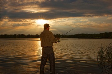 Angler standing in the lake fishing at sunset with lens flare defect.