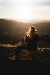 Girl with winter clothes and hair in the wind sitting on a wall looking at a beautiful and warm sunset in a mountainous environment in Alava, Basque Country