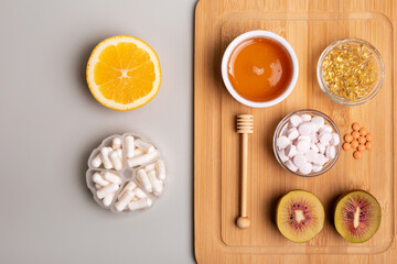 Fototapeta na wymiar Natural vitamins from fruits and honey and vitamin pills, organic minerals in small bowls from above on wooden desk on light background. Orange, kiwi and honey as sources of natural vitamins.