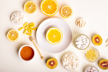 Many jars filled with dietary supplements, vitamins and minerals in form of pills, capsules and tablets. Orange on white round plate, honey and kiwi from above on light background. Healthy lifestyle.