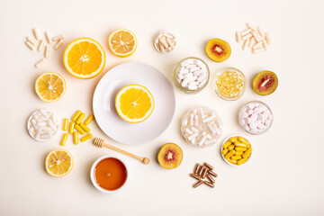 Many jars filled with dietary supplements, vitamins and minerals in form of pills, capsules and tablets. Orange on white round plate, honey and kiwi from above on light background. Healthy lifestyle.