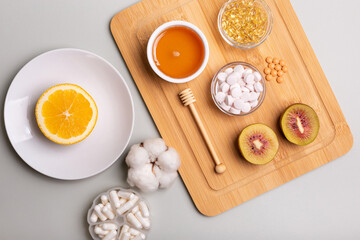 Natural vitamins from fruits and honey and vitamin pills, organic minerals in small bowls from above on wooden desk on light background. Orange on plate, kiwi and honey as sources of natural vitamins.