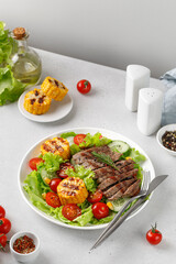 Roast beef salad on white plate and grey background. Salad, meal with meat steak, grilled corn and beef meat with vegetable. Diet dinner concept.