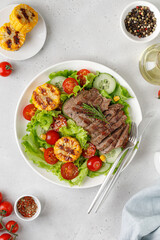 Salad, meal with meat steak, grilled corn and beef meat with vegetable. Roast beef salad on white plate and grey background.