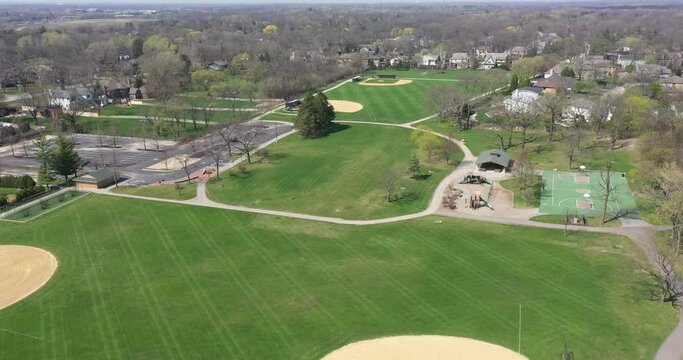 Aerial view of a large suburban park with baseball and soccer fields, basketball court and playground in early spring.