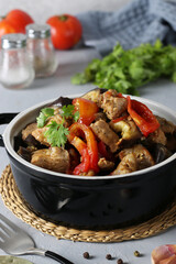 Braised pork with eggplant and tomatoes in a ceramic dish on gray background, Closeup