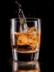 Cognac splashes in a transparent glass on a dark background.