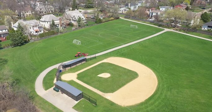 Aerial view of a baseball and soccer field in a large suburban park with a sports field mower tractor grooming the grass in early spring.