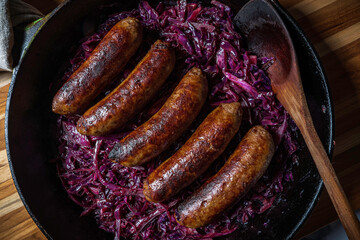 Beer-braised bratwurst sausages with red cabbage and onion in a cast-iron skillet.