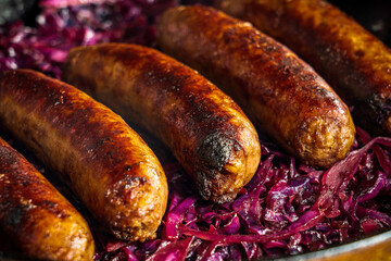 Beer-braised bratwurst sausages with red cabbage and onion in a cast-iron skillet.