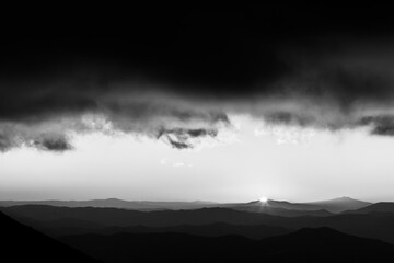 Distant sunset above layers of mountains and valleys with mist and fog, with a rooftop of close red clouds