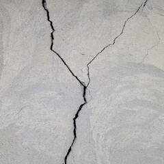 Large uneven vertical cracks on a gray plastered surface. A cracked concrete wall covered with...