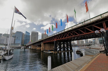 Cyclist-pedestrian Pyrmont Bridge across Cockle Bay, Darling Harbour, huge national flag-CBD skyline. Sydney-Australia-609