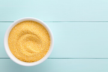 Raw coarsely ground cornmeal or polenta in white bowl, photographed overhead on blue wood with copy space on the side (Selective Focus, Focus on the cornmeal) - obrazy, fototapety, plakaty