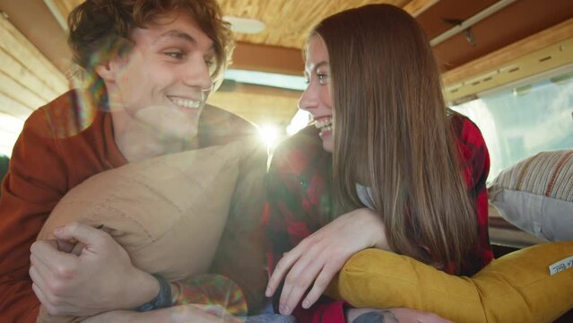 Young couple lie in a cozy mini camper bus and talk. Sweet youth love. Romantic atmosphere. Nature helps strengthen relationships. Communication concept. Carly hair boy and girl with tattoos