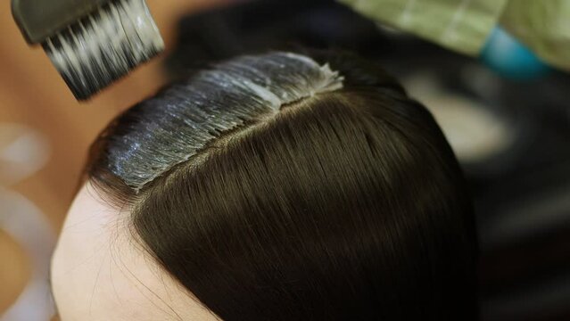 close up painting a brunette with hair dye with a paint brush in a beauty salon