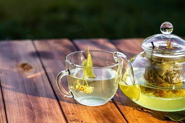 cup of hot linden tea with spoon and linden flowers on wooden table in a garden