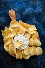 Vertical image beautiful potato chips and sauce in a white bowl on a wooden cutting board.