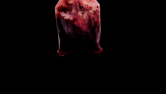 Red and wet tea bag on a black background