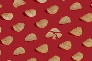 Pattern of potato chips with one crushed chip in the middle on red backround.