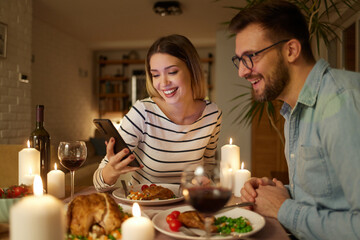 Happy couple enjoying food and wine while surfing the net on smart phone