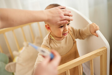 Mother checking body temperature of her baby boy with a thermometer