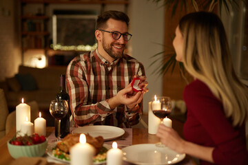 Delighted woman looking at her boyfriend while getting a marriage proposal over romantic dinner at home