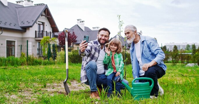 Son and grandson sitting in garden and taking selfie photo. Planting trees concept. Making picture of three generations.
