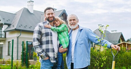 Portrait of happy three generations of family. Man with old father and cute little son in garden after planting work. Cheerful grandfather with son and grandson at summertime house.