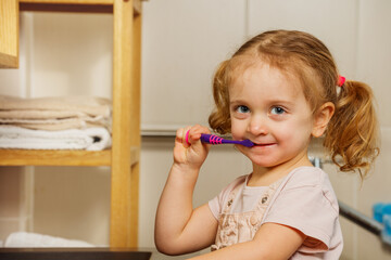 Cute curly girl brush teeth with toothbrush in the bathroom