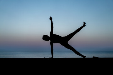 Silhouette de femme faisant du yoga devant la mer au coucher de soleil, posture Ardha Chandrasana...