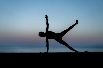 Silhouette de femme faisant du yoga devant la mer au coucher de soleil, posture Ardha Chandrasana (Half-Moon Pose - Demi-lune)