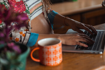 Close-up of a pregnant woman in colorful clothes working from home on a laptop.
