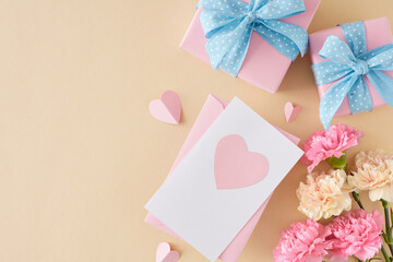 Trendy Mother's Day gift concept. Top view photo of envelope postcard gift boxes pink cream carnation flowers and paper hearts on light beige background. Flat lay with empty space for greeting