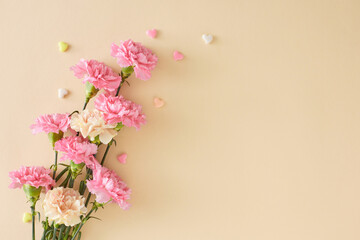 Fototapeta na wymiar Mother's Day floral gift concept. Top view photo of bunch of pretty carnation flowers and small hearts on light beige background. Flat lay with empty space for your message or advert
