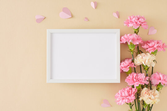 Charming Mother's Day flower gift concept. Top view photo of bunch of pink white carnation and pink paper hearts on light beige background. Flat lay with white frame for greeting text or advert