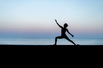 Silhouette de femme faisant du yoga devant la mer au coucher de soleil,  posture Virabhadrasana (Warrior - Guerrier)