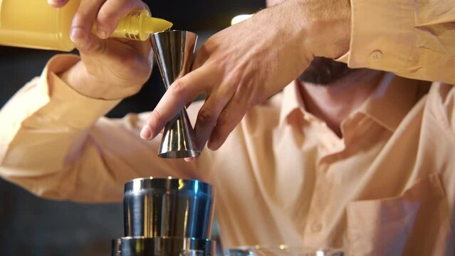 Professional bartender masterly creating a cocktail in modern bar. Experienced barman adding syrip into shaker using jigger - food and drink