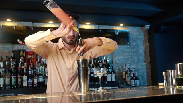 Professional bartender masterly creating a cocktail in modern bar. Experienced barman adding syrip into shaker using jigger - food and drink