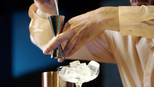 Professional bartender masterly creating a cocktail in modern bar. Experienced barman adding syrip into shaker using jigger - food and drink