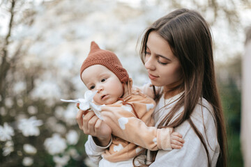 A teenage girl is showing her newborn sister a flower from a magnolia tree in a blooming garden.