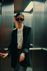 Stylish woman in black jacket and sunglasses posing in elevator, fashion model, dark cinematic light and color