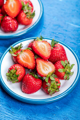 Fresh strawberries on white plates, on blue wooden background.