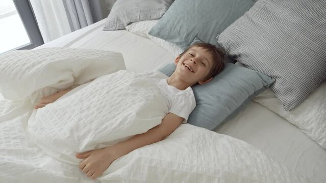 A young boy jumps out from under his blanket, laughing with a sense of playfulness and merriment that shines through in his expression