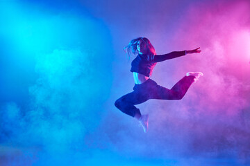 Fototapeta na wymiar a girl in dark clothes dances on a neon background in smoke, modern dance