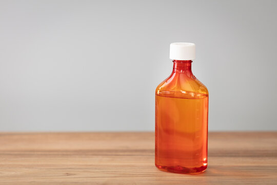 Bottle with liquid medicine. Transparent orange vial with lid on neutral background. Stop your cold today. Copy space for text or image.